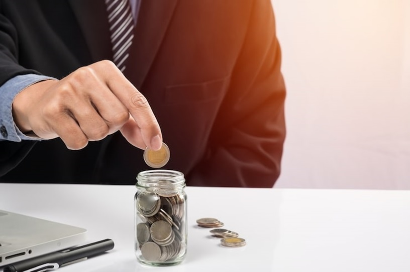 A person dropping a coin into a jar.